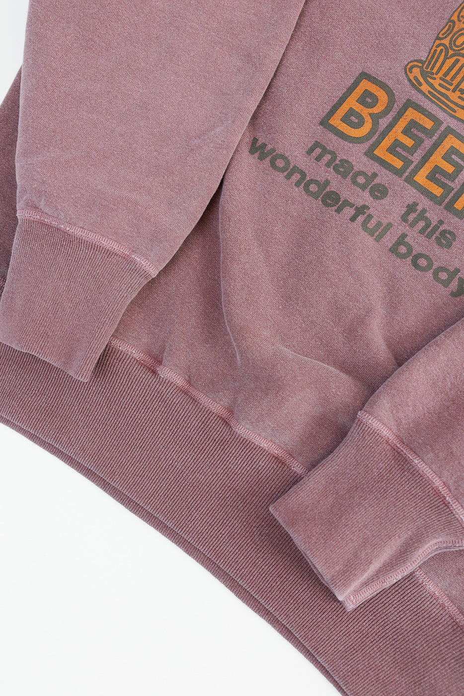 Close-up of front lower section of faded bordeaux print sweatshirt, showing ribbed hem and sleeve cuff details, partial text graphic, and soft fabric texture.