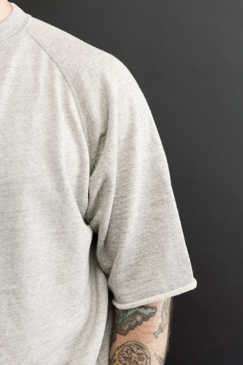 Close-up of male model's left shoulder and sleeve, showcasing heather gray crewneck texture and hem detail
