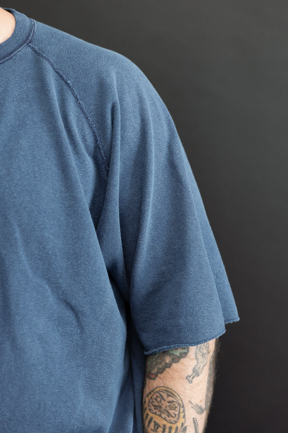 Close-up of male model's left side showing blue t-shirt with raglan sleeve and raw hem, athletic build