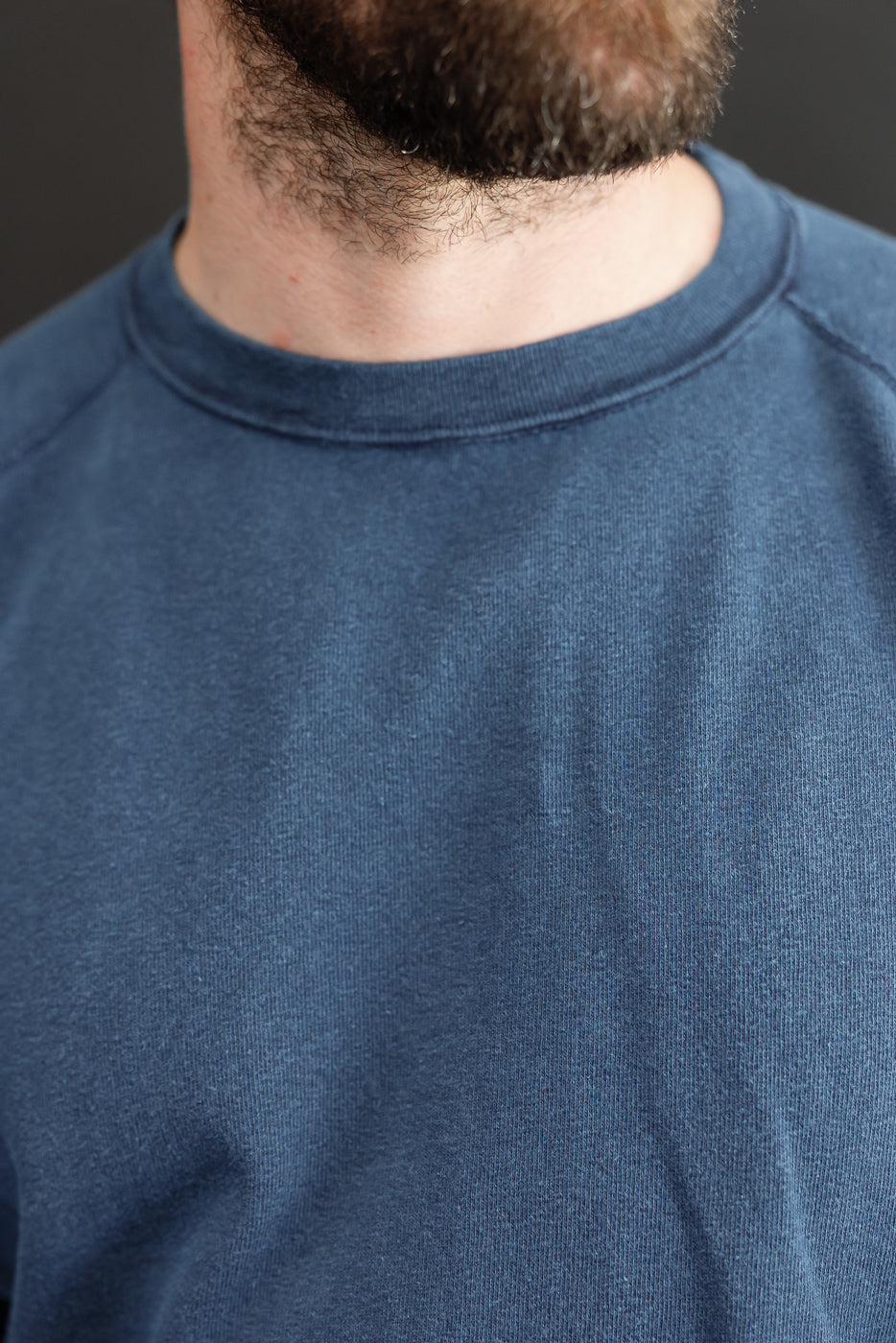 Close-up front view of navy crewneck sweatshirt on male model, showcasing soft fabric texture and ribbed collar.