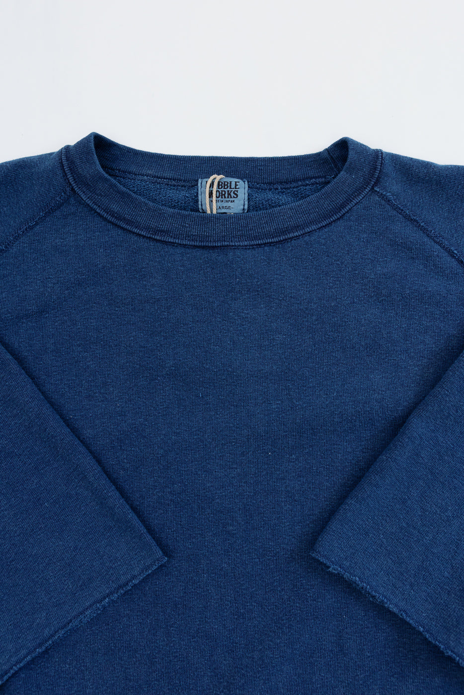 Close-up front view of navy raglan sweatshirt, ribbed crew neck, visible 'Bible Works' tag, soft textured fabric