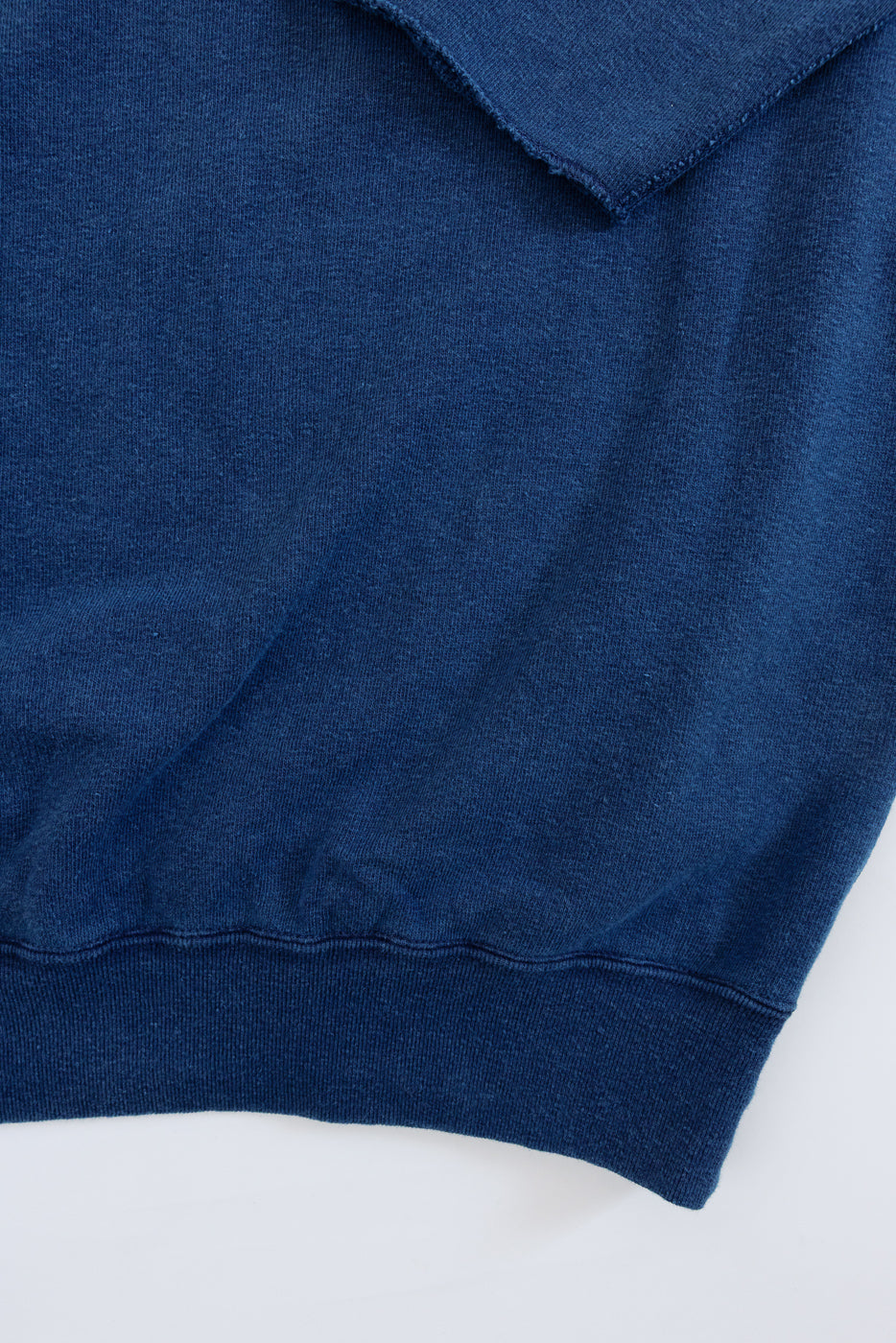 Close-up of navy blue sweatshirt hem and side seam, showing ribbed knit texture and clean stitching detail