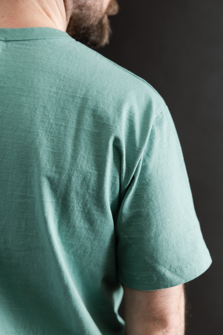 Close-up of back right shoulder of emerald green midweight tee on male model, athletic build