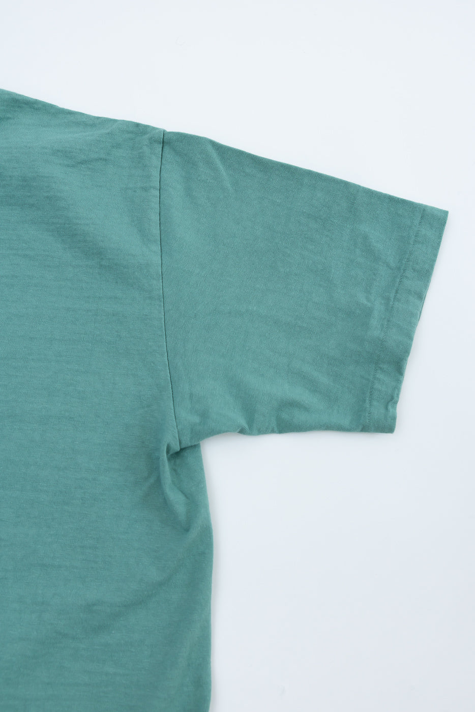 Close-up of Dant emerald green fallen cotton tee, flat lay, showing right sleeve and side seam.