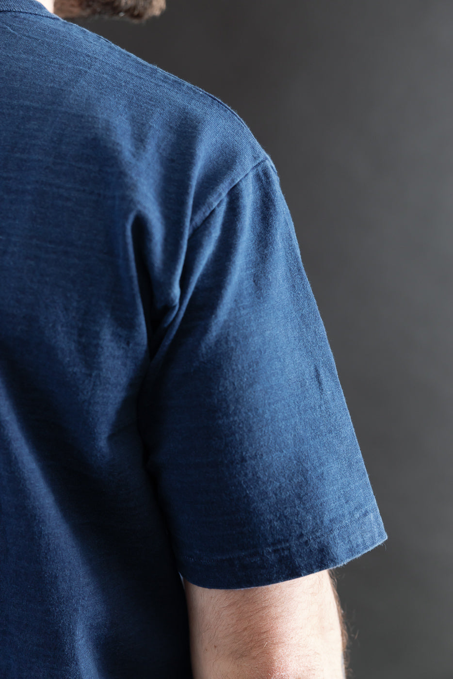 Close-up of male model's right shoulder in Dubble Works indigo midweight tee, side view, showing short sleeve and cotton texture.