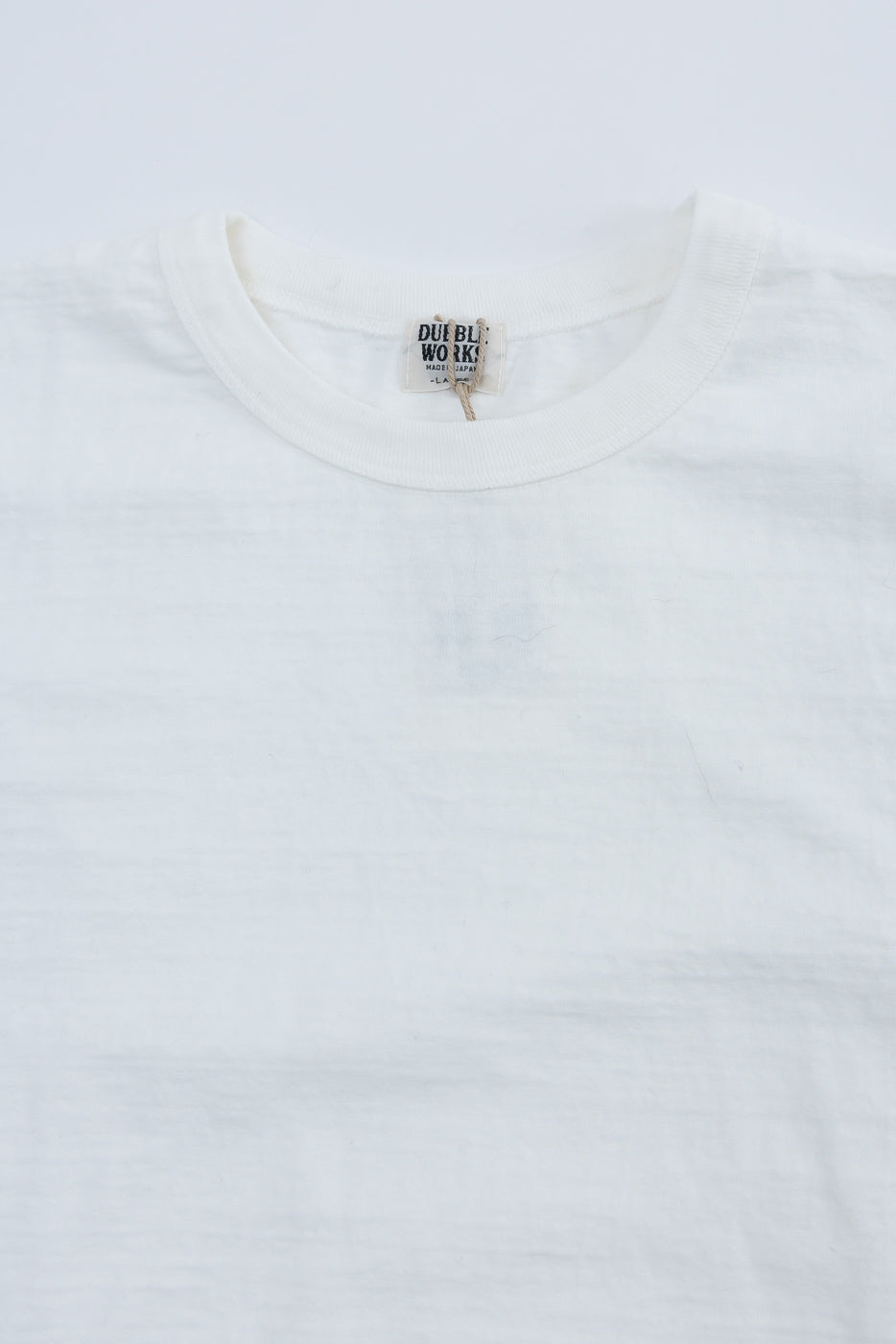 Close-up of Dubble Works off-white cotton tee front neckline, showing fabric texture and tag detail.