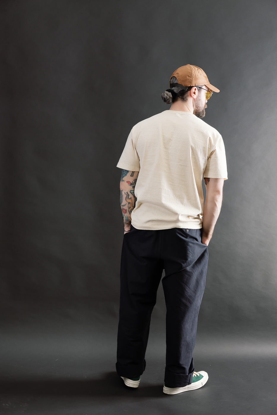 Male model 5'9 165lbs athletic build, back view full body, cream Dubble Works tee, dark pants, casual streetwear style at Dant