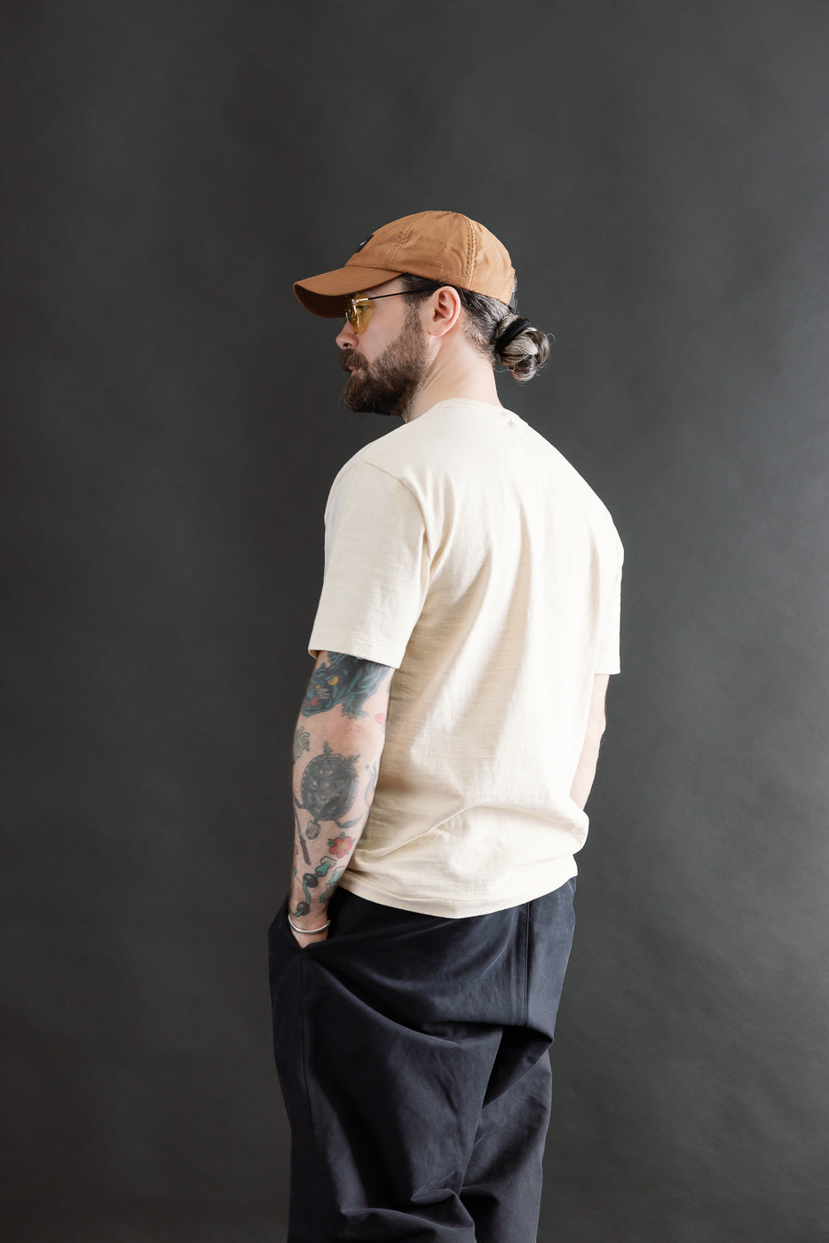 Male model 5'9, 165lbs athletic build wearing Dubble Works cream tee, side back view, short sleeves, casual fit