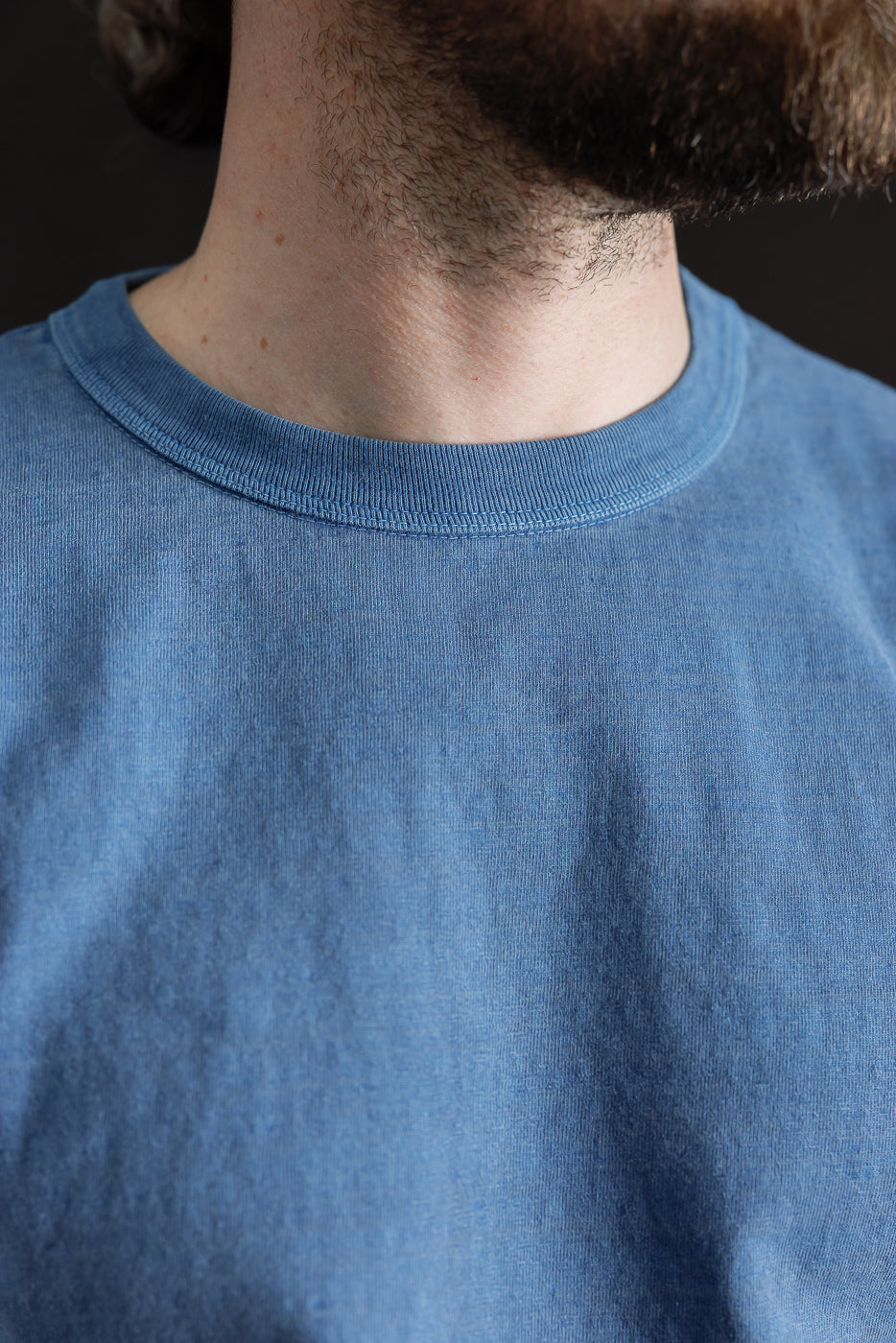 Close-up of a male model wearing a light indigo Dubble Works Fallen Cotton midweight tee, showing the front collar and fabric texture.