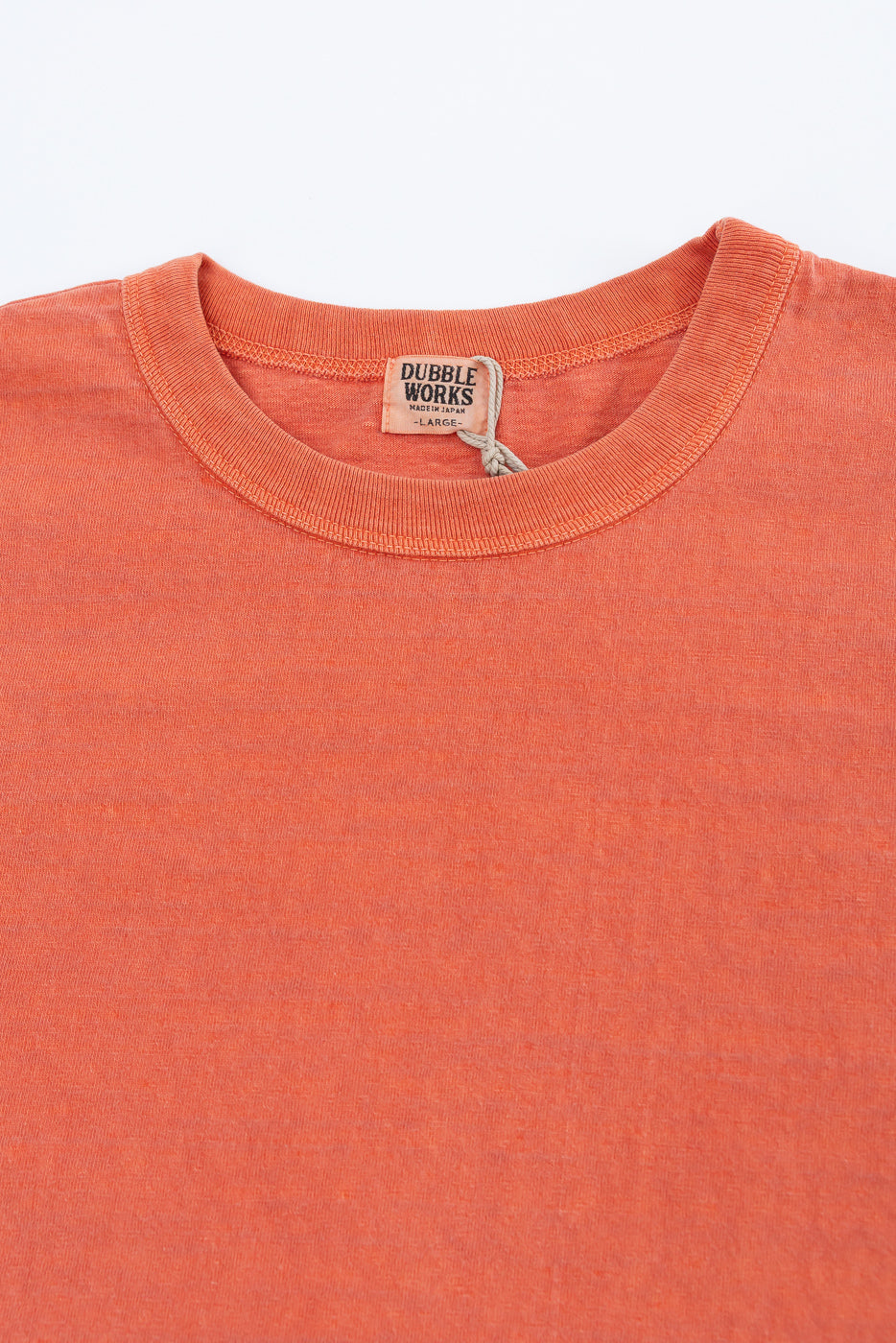 Close-up of Dubble Works Fallen Cotton orange tee front, showing collar, tag, fabric texture.