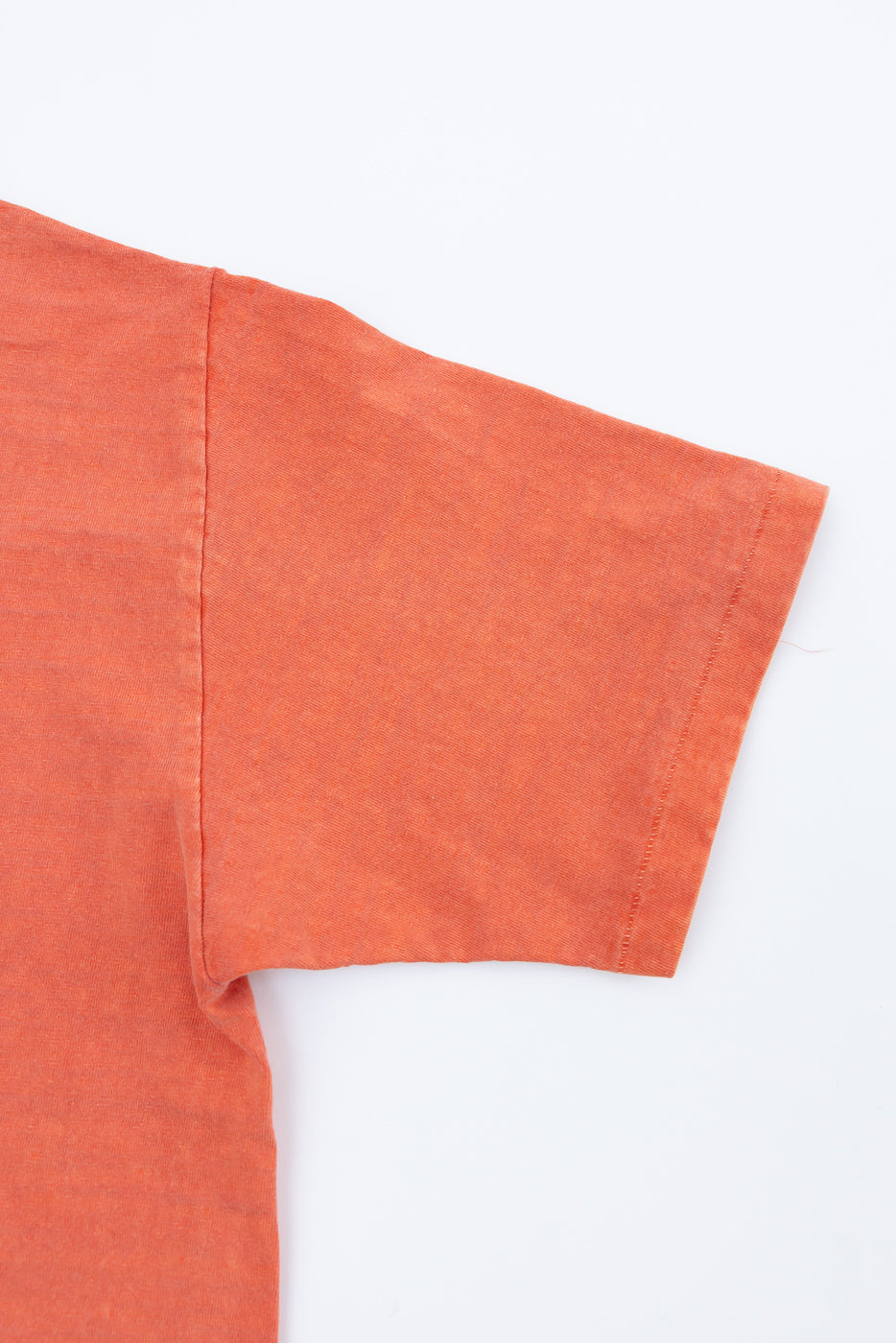 Close-up of Dubble Works orange midweight tee sleeve, front left side, showing fabric texture and stitching detail.