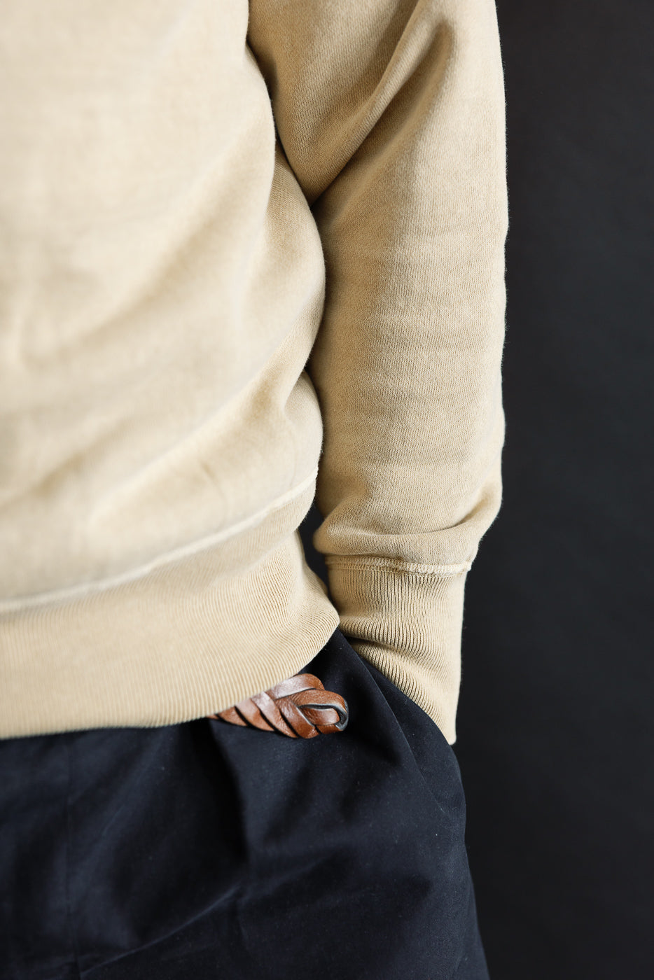 Close-up of male model’s right side in beige faded sweatshirt, ribbed hem and sleeve cuff detail, hand in pocket