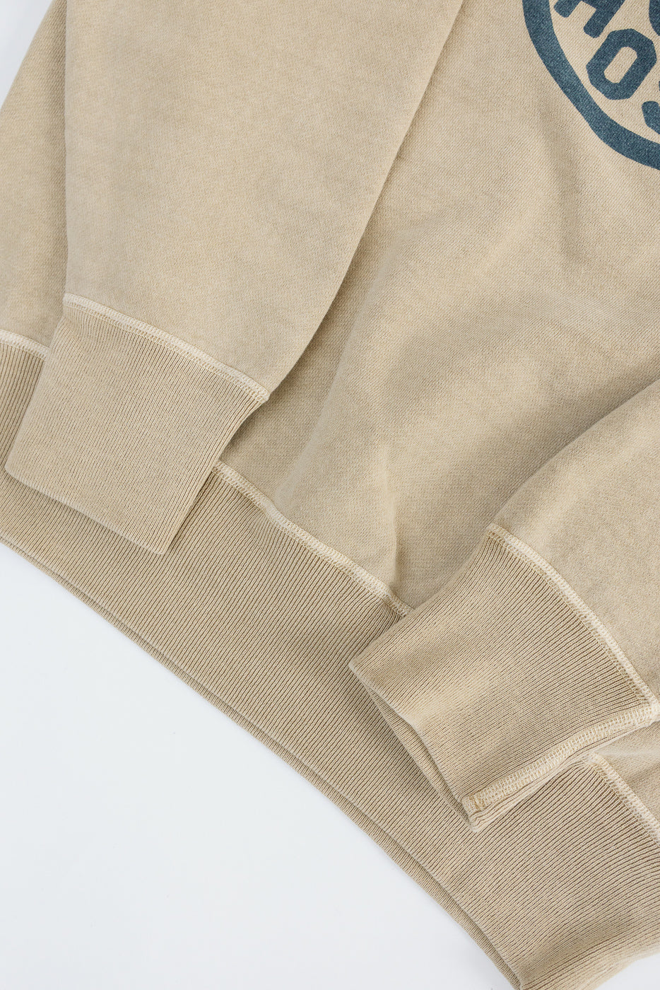 Close-up of front waistband and sleeve cuffs on beige faded print sweatshirt, ribbed hem detail