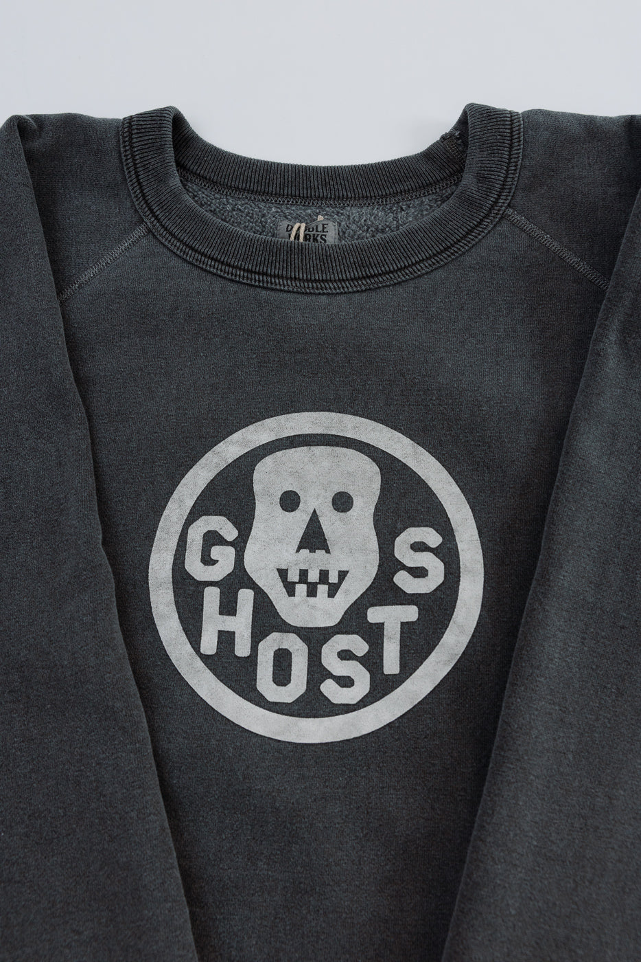 Close-up of front chest on faded black crewneck sweatshirt showing 'GHOSTS' skull graphic and ribbed collar.