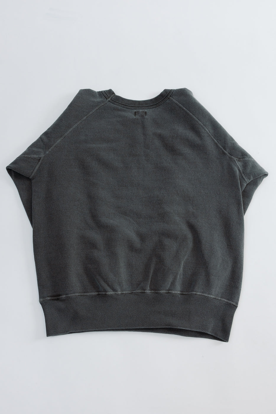 Flat lay of faded black sweatshirt, back view, showing raglan sleeves and ribbed hem.