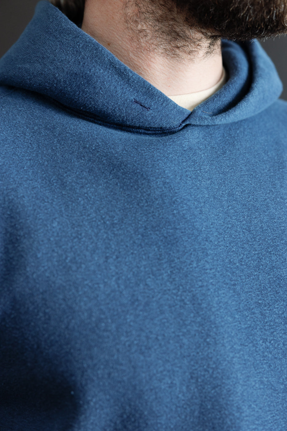 Close-up of indigo-dyed hoodie front, fabric texture and hood detail on male model, athletic build.