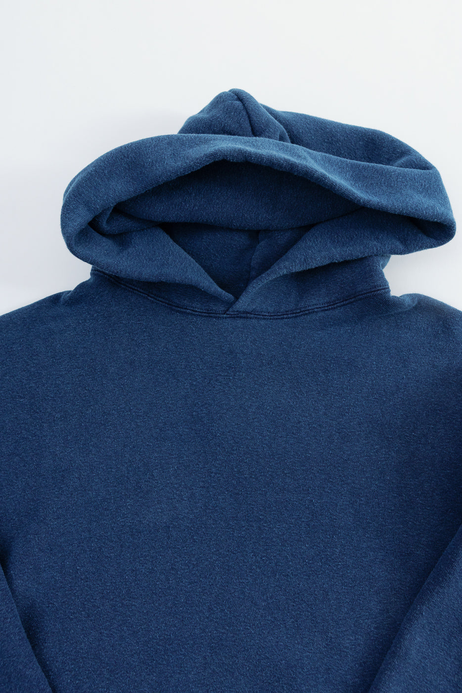 Close-up of indigo-dyed loopwheel sweatshirt hoodie, front upper section showing hood and texture.