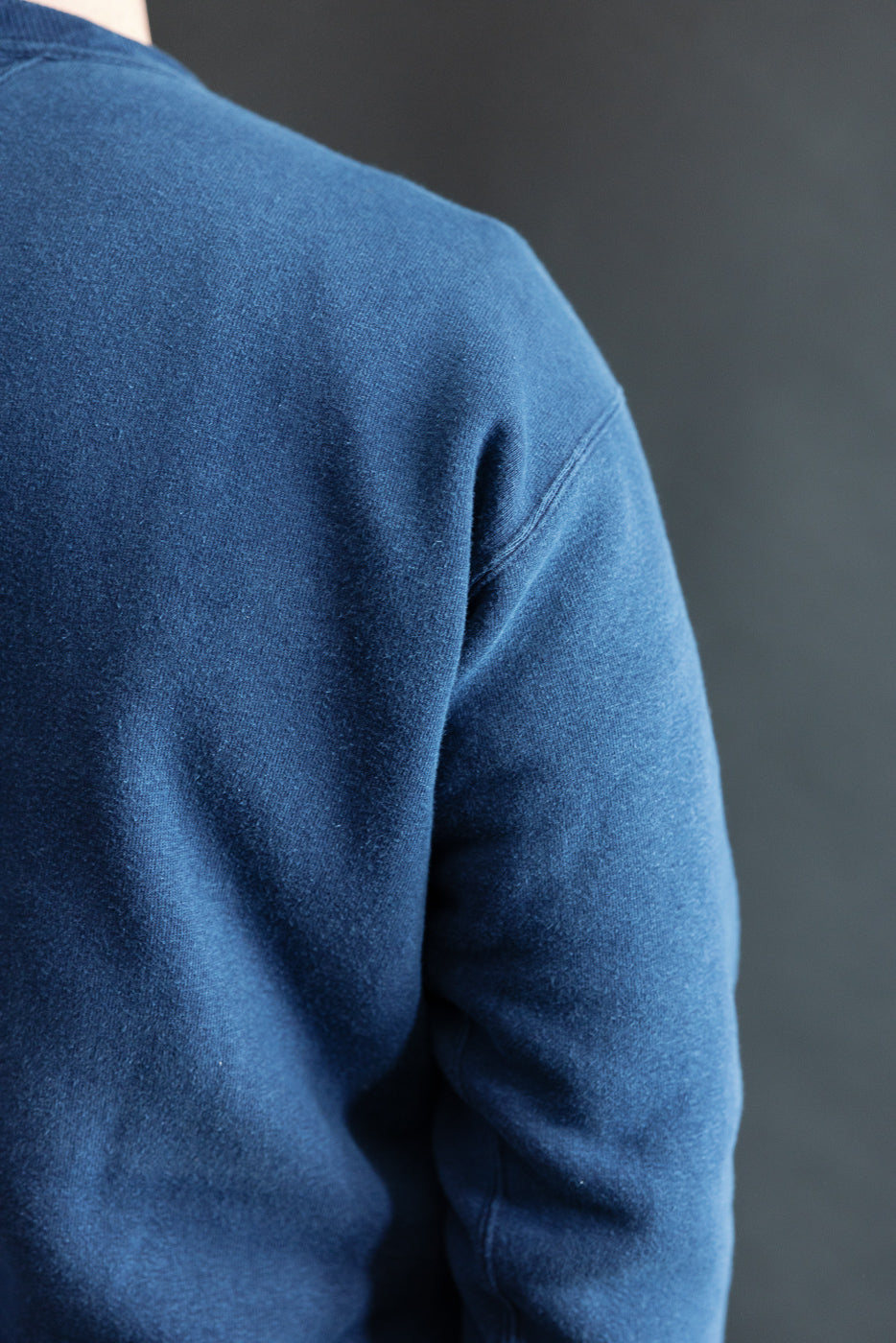 Close-up of male model's back left shoulder wearing indigo dyed loopwheel sweatshirt, showcasing fabric texture.
