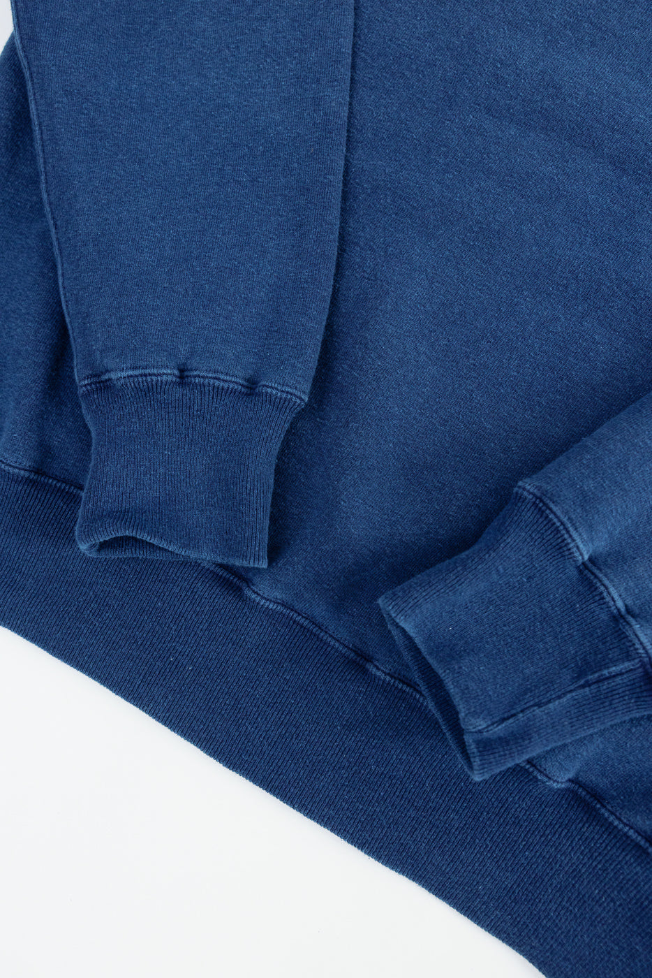 Close-up of indigo-dyed loopwheel sweatshirt front, showing ribbed cuffs and hem detail.