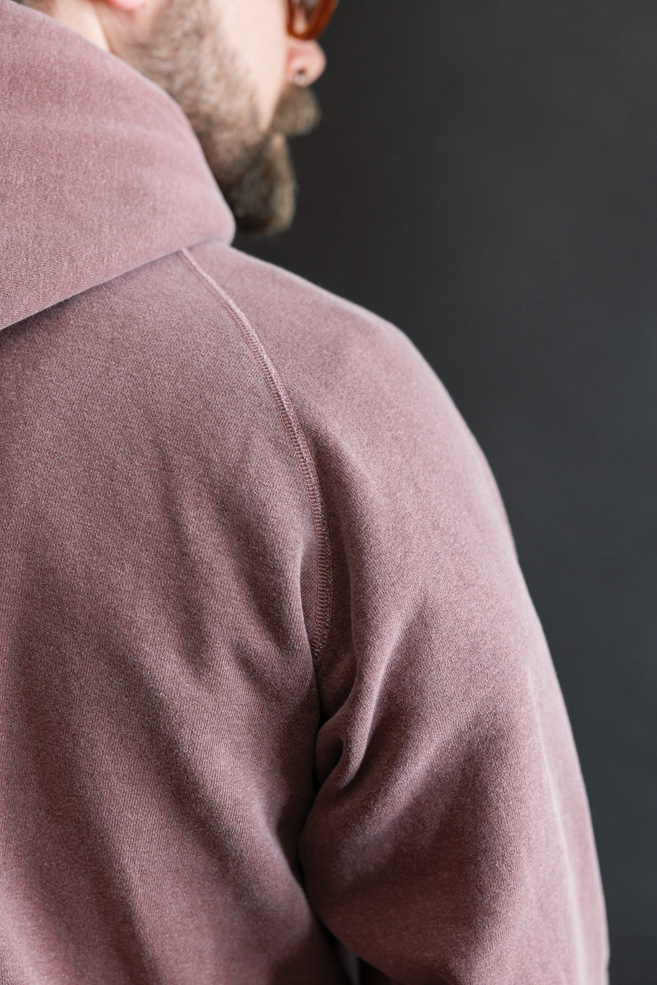 Close-up of male model's upper back and shoulder, showing bordeaux hoodie fabric and stitching. Model is 5'9