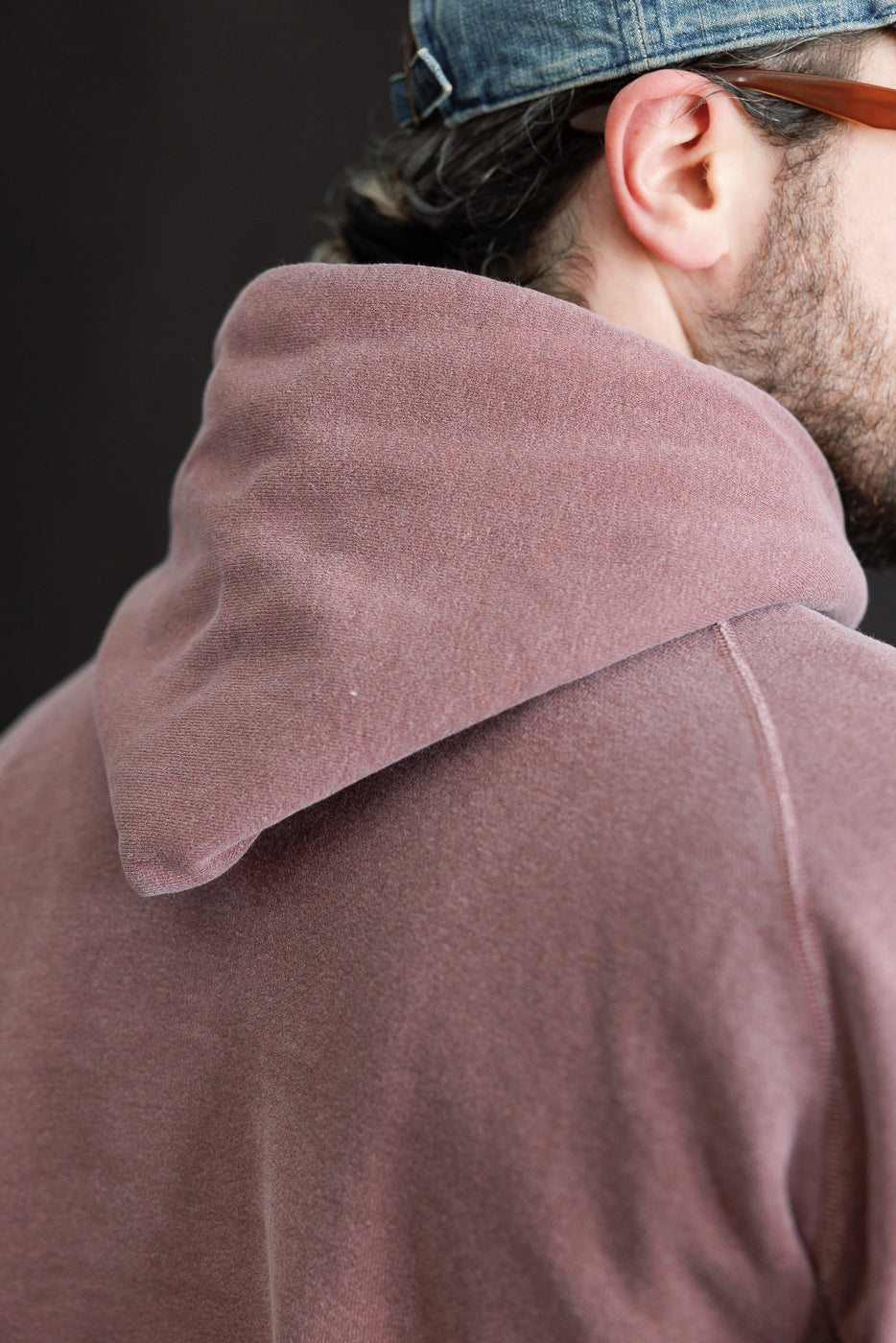 Close-up of the back hood and shoulder seam on a faded bordeaux men's hoodie, male model 5'9
