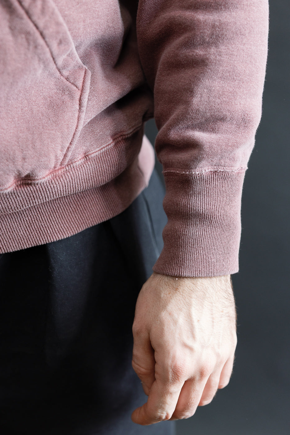 Close-up of male model's right side, showing faded bordeaux hoodie sleeve cuff and hem detail. Model is 5'9