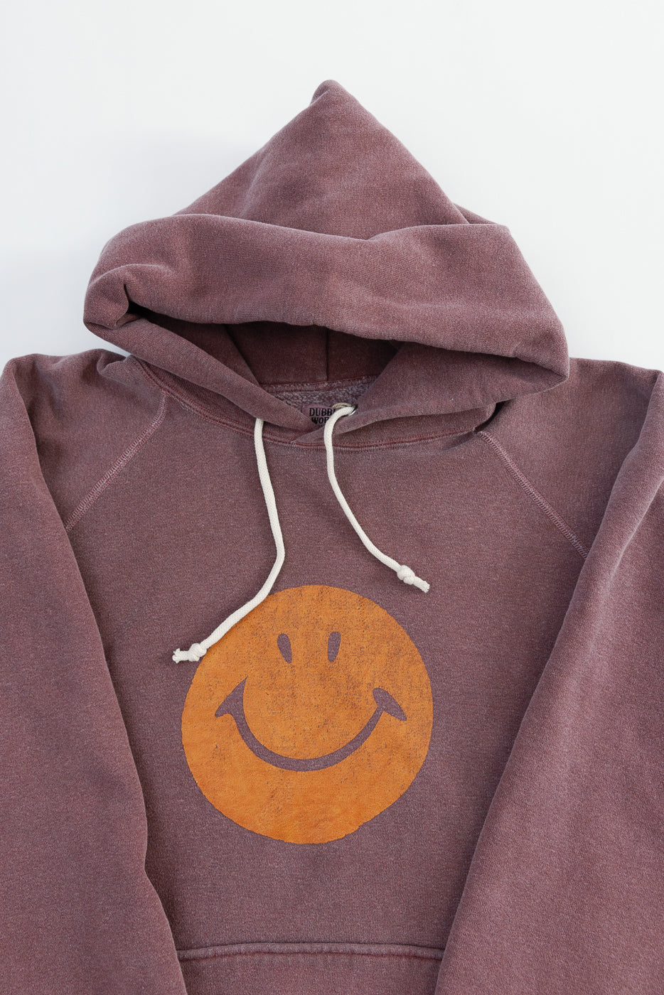 Close-up of front of faded bordeaux hoodie with orange smiley face print, hood and drawstrings visible