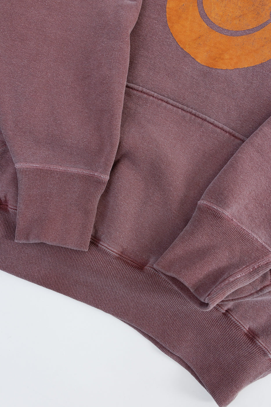 Close-up of front hem and sleeve cuffs on faded burgundy print hoodie, showing fabric texture.