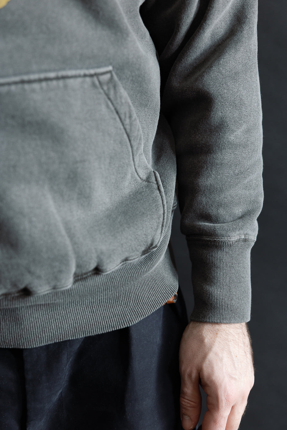 Close-up of front pocket, sleeve cuff, and hem on faded black hoodie, male model, right side