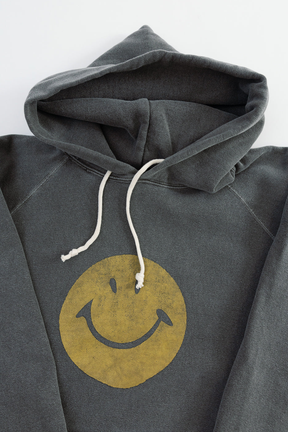 Close-up front view of faded black hoodie with yellow smiley face print, drawstring hood.