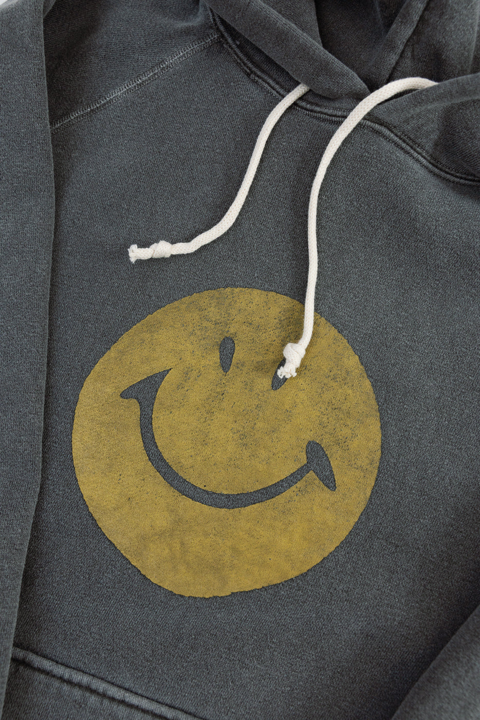 Close-up front view of faded charcoal hoodie with yellow smiley face print and white drawstrings.