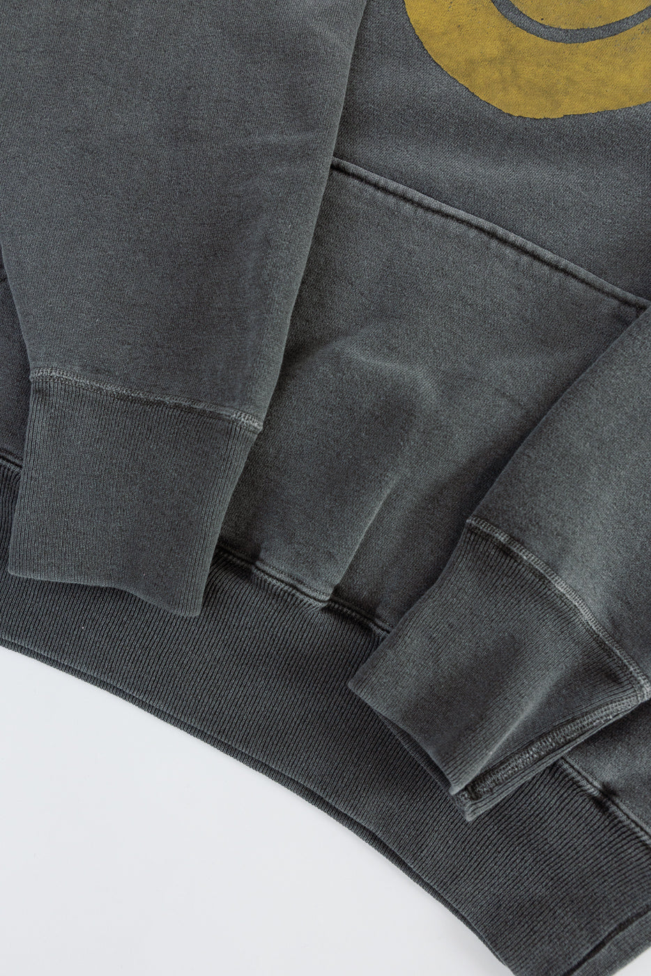 Close-up of front hem, cuffs, and kangaroo pocket on faded black print hoodie, showing fabric texture.