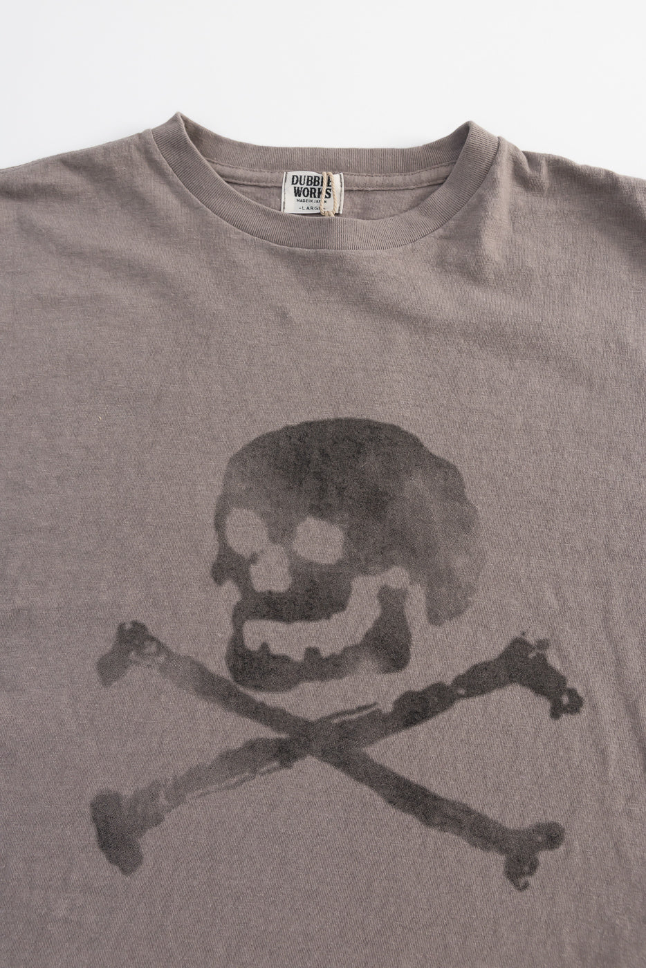 Gray crew-neck T-shirt featuring a large, weathered skull-and-crossbones motif on the front. The DUBBLE WORKS Raffy Tenjiku design combines vintage inspiration with unique Japanese slub jersey fabric and seamless tubular construction.
