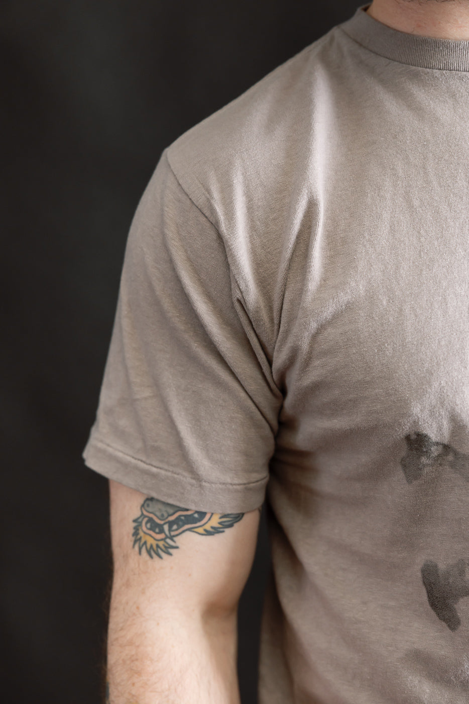 Close-up of the 5.4oz - Raffy Tenjiku Printed T-Shirt Skull & Crossbone in Grey, showcasing its vintage-inspired slub jersey texture and tubular knit design, with a tattoo visible under the sleeve.