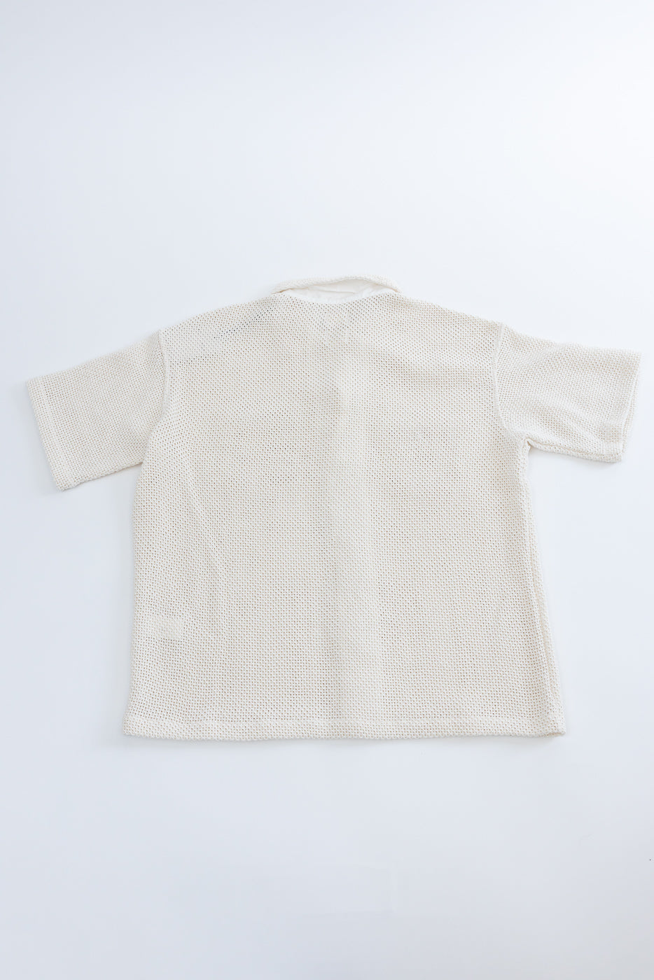 Flat lay of short sleeve ecru cotton shirt, back side, showing mesh texture and straight hem.