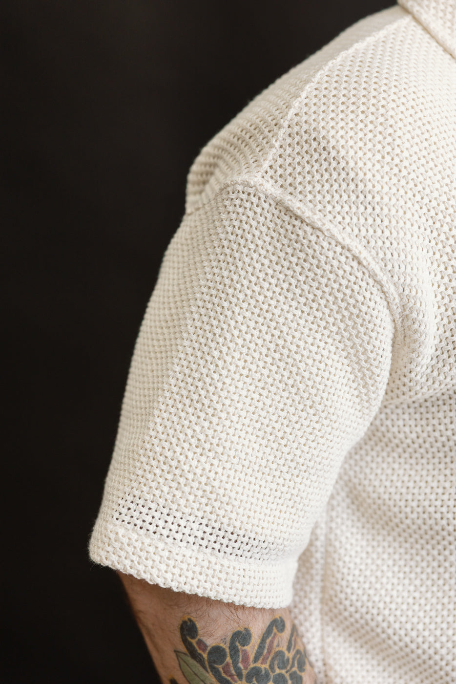 Close-up of male model's right arm in ecru cotton shirt, showing textured short sleeve fabric and stitching detail.