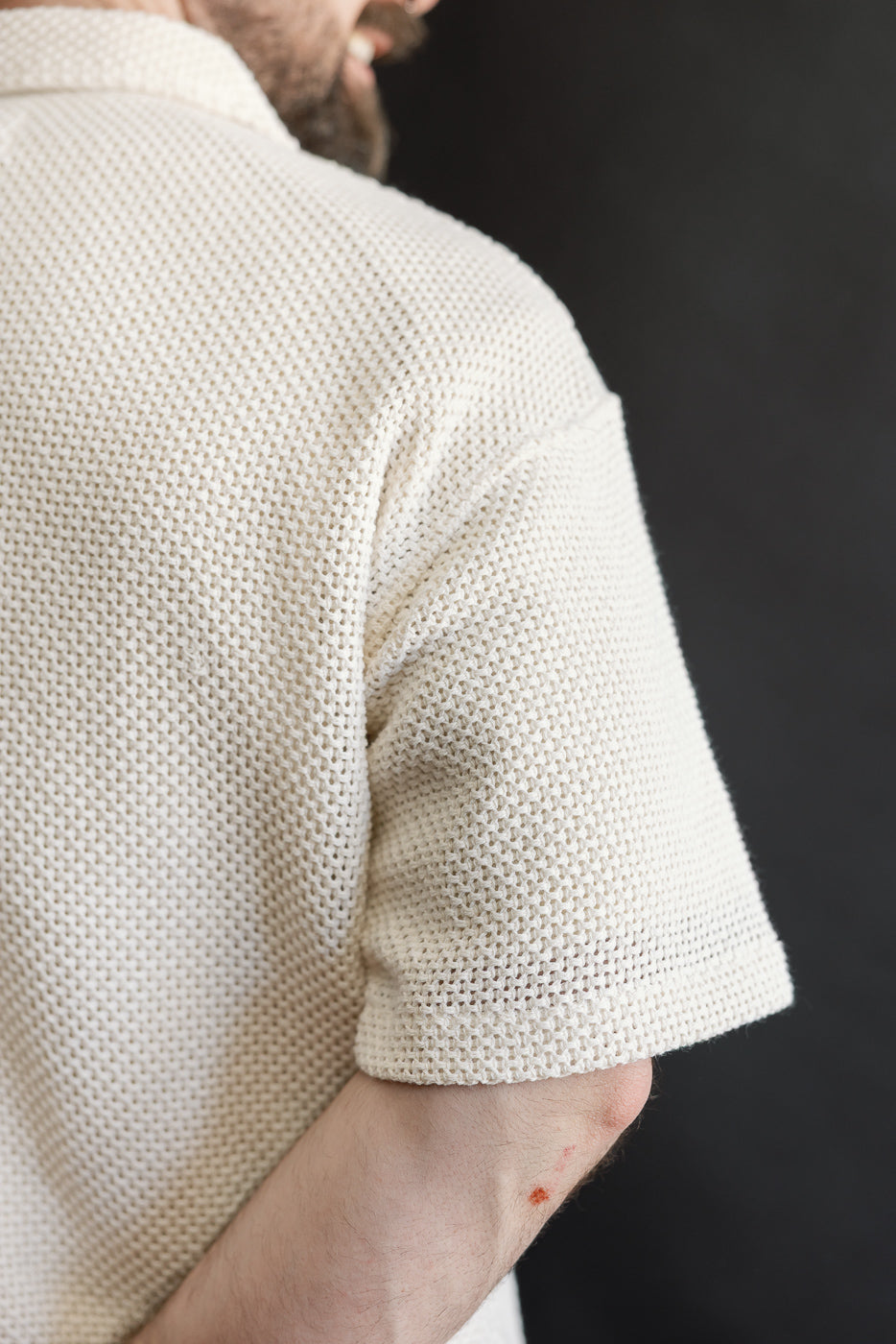 Close-up of back right shoulder and sleeve of ecru cotton textured shirt on male model, 5'9