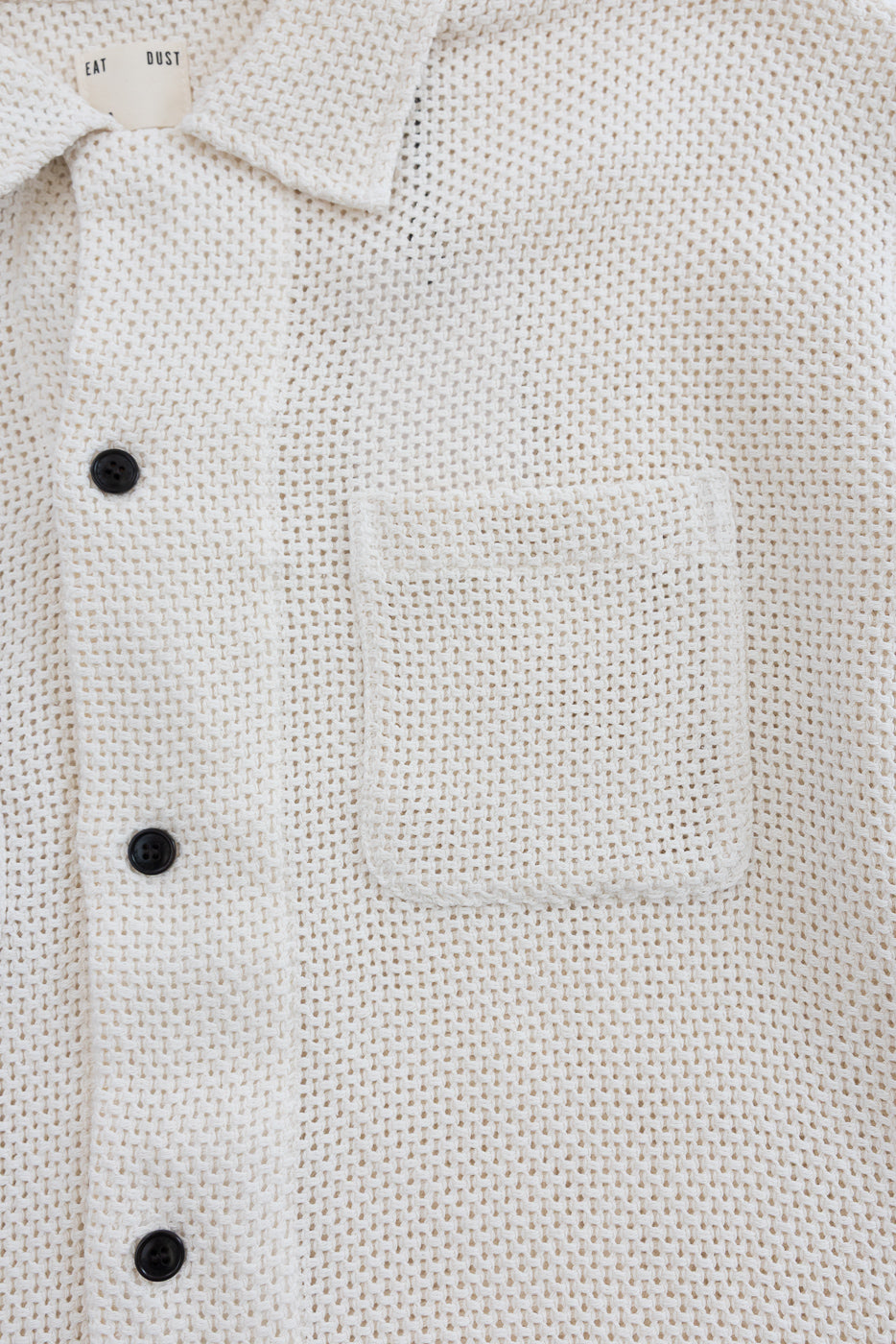 Close-up of front chest area of ecru cotton shirt, showing texture, buttons, collar, and pocket.