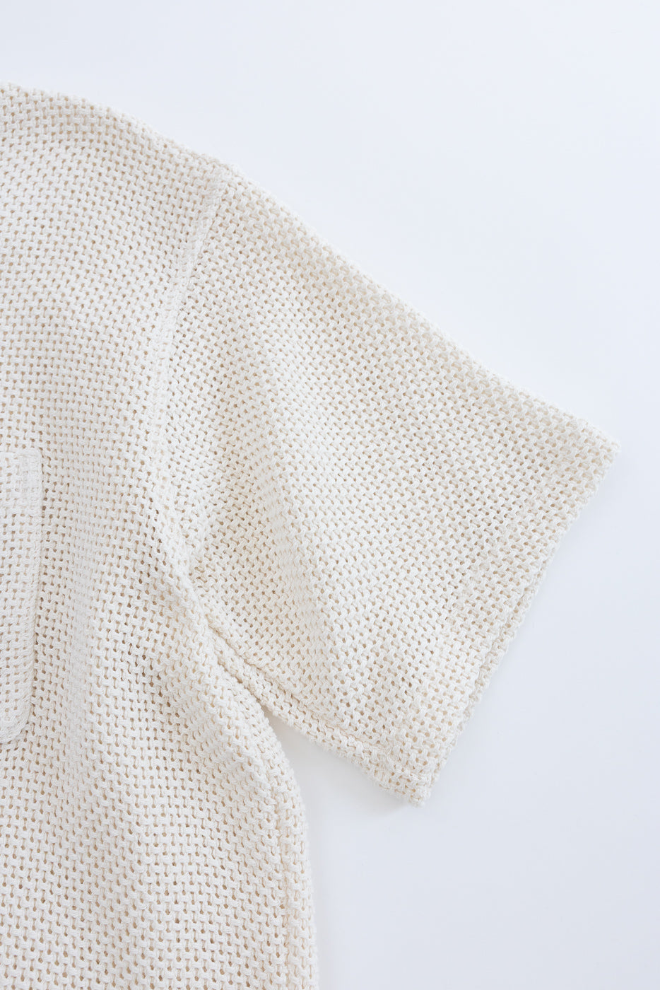Close-up of short sleeve ecru cotton shirt, showcasing textured knit fabric and left side seam.