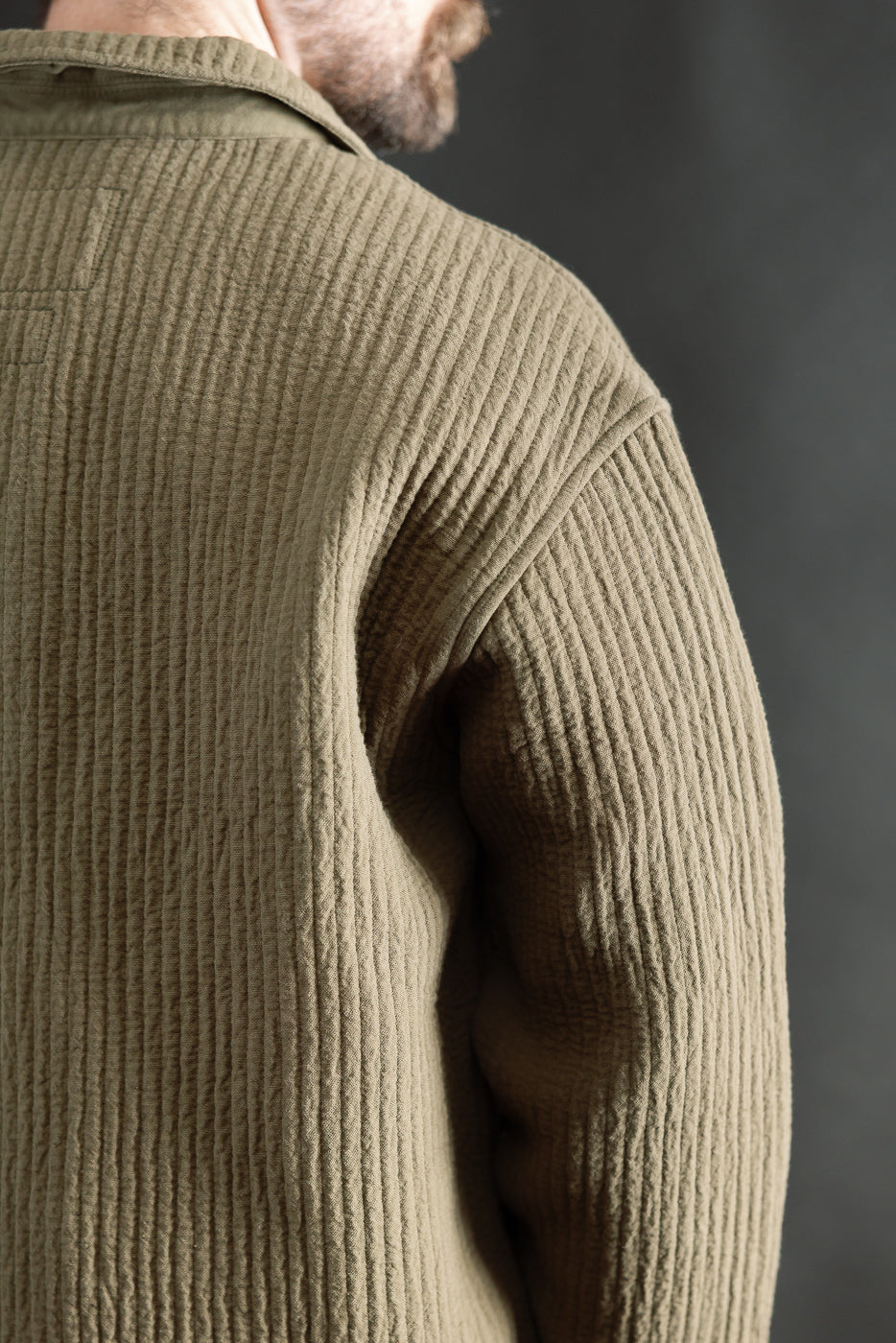 Close-up of male model's back wearing fossil green jacquard shirt, textured fabric, collar detail, Dant contemporary casual apparel. Model is 5'9