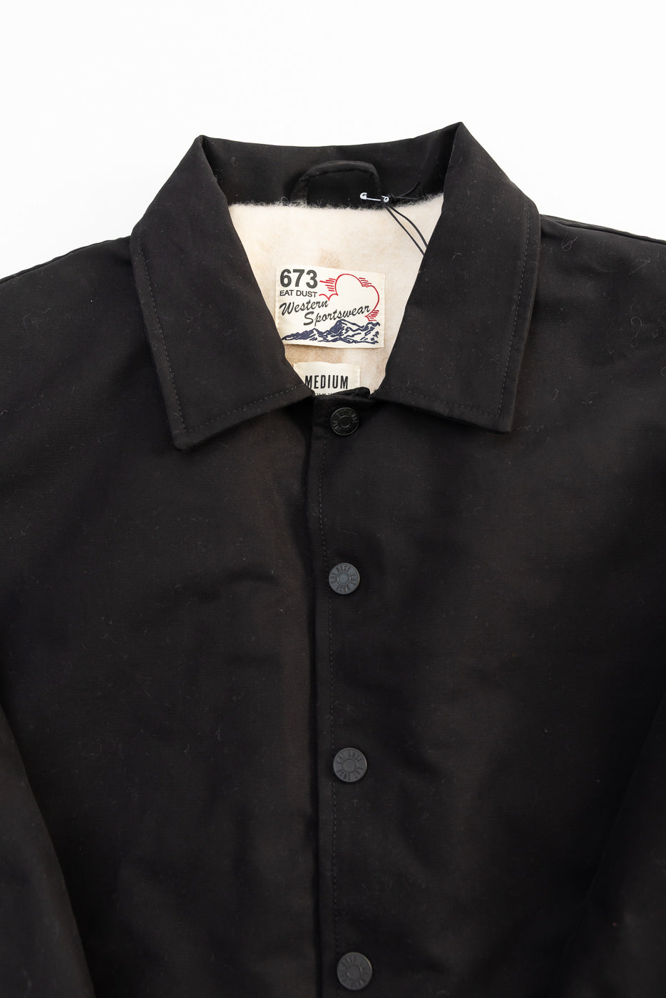 Close-up front of Eat Dust Dago jacket, black cotton, lined collar, unique tag, buttons.