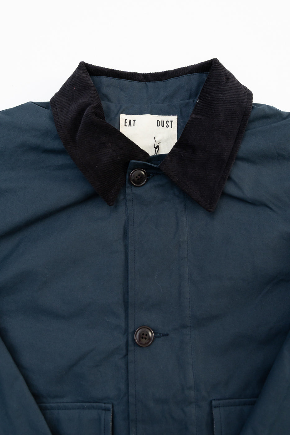 Close-up front of Eat Dust dry wax cotton jacket, black corduroy collar, visible buttons, tag detail