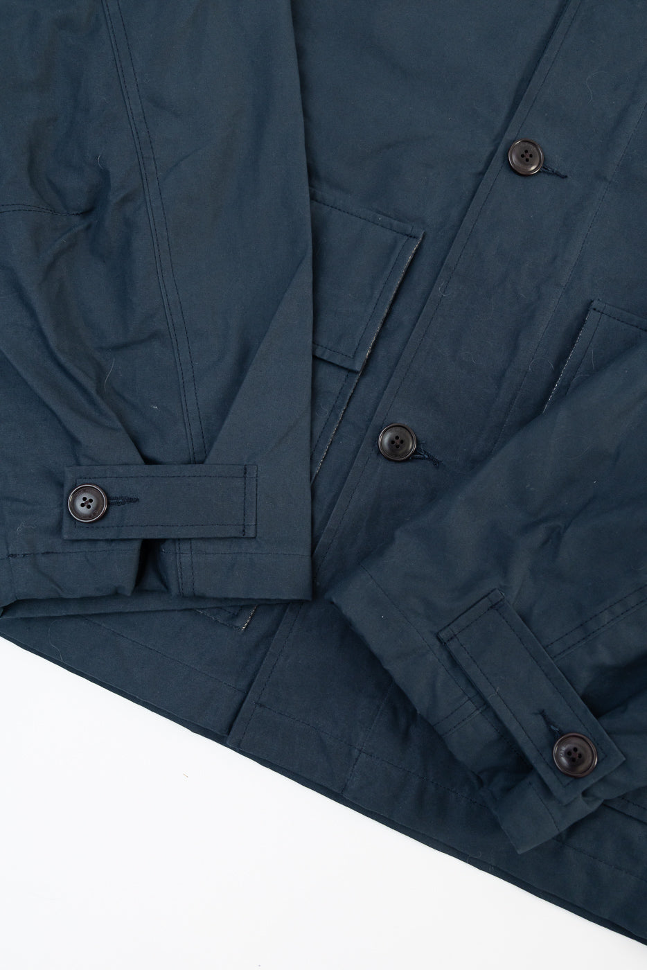 Close-up of Eat Dust Creek dry wax cotton jacket, front side, showing navy fabric, buttons, cuff details, and stitching.