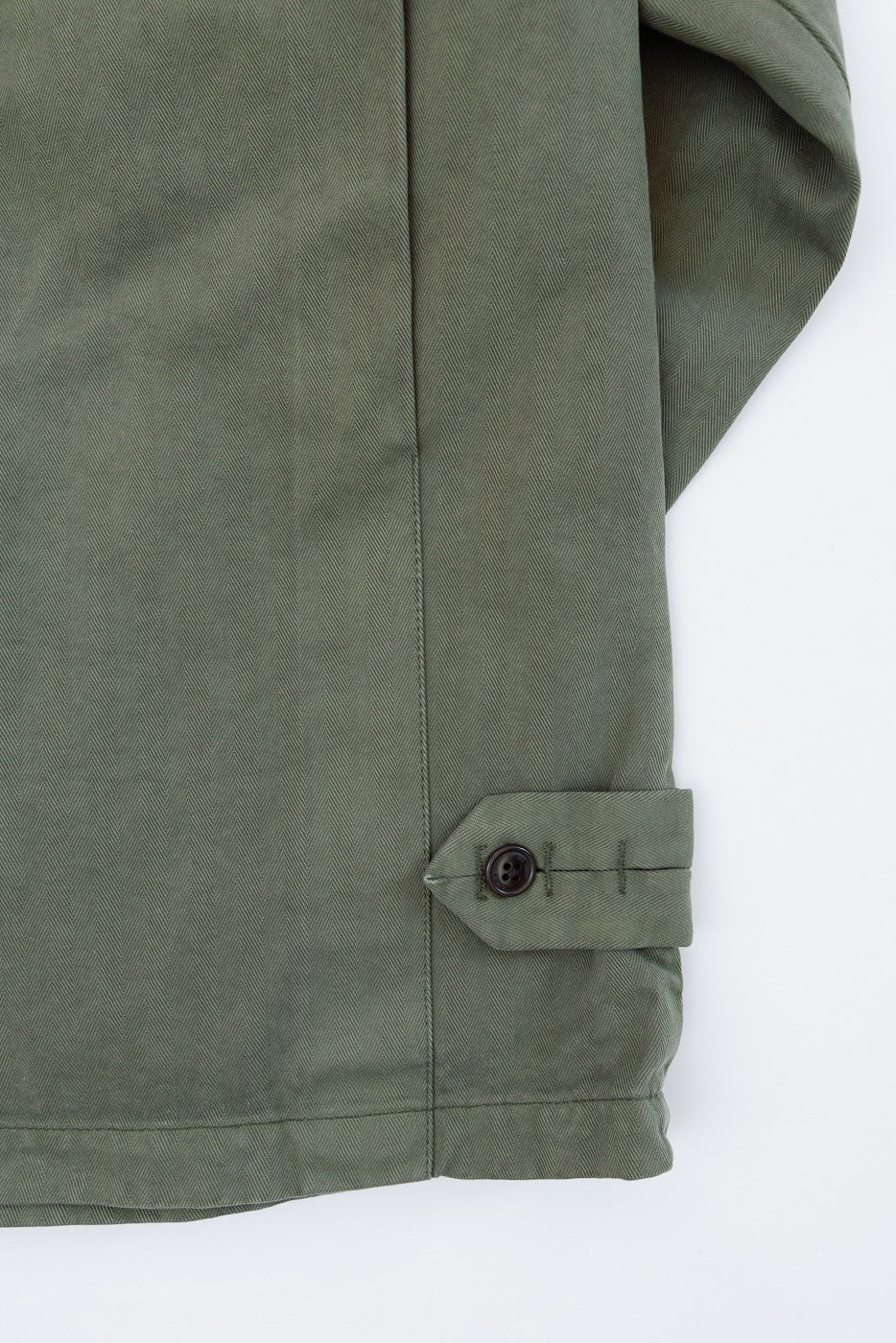 Close-up of the right sleeve cuff detail on olive green twill trousers, showing a buttoned tab.