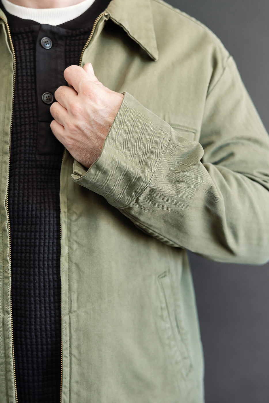 Close-up front view of an olive green canvas jacket sleeve and zipper detail.