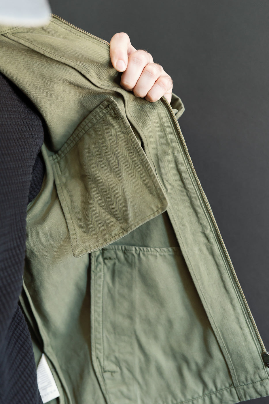 Close-up of the front interior of an olive green utility jacket showing pocket detail and fabric.