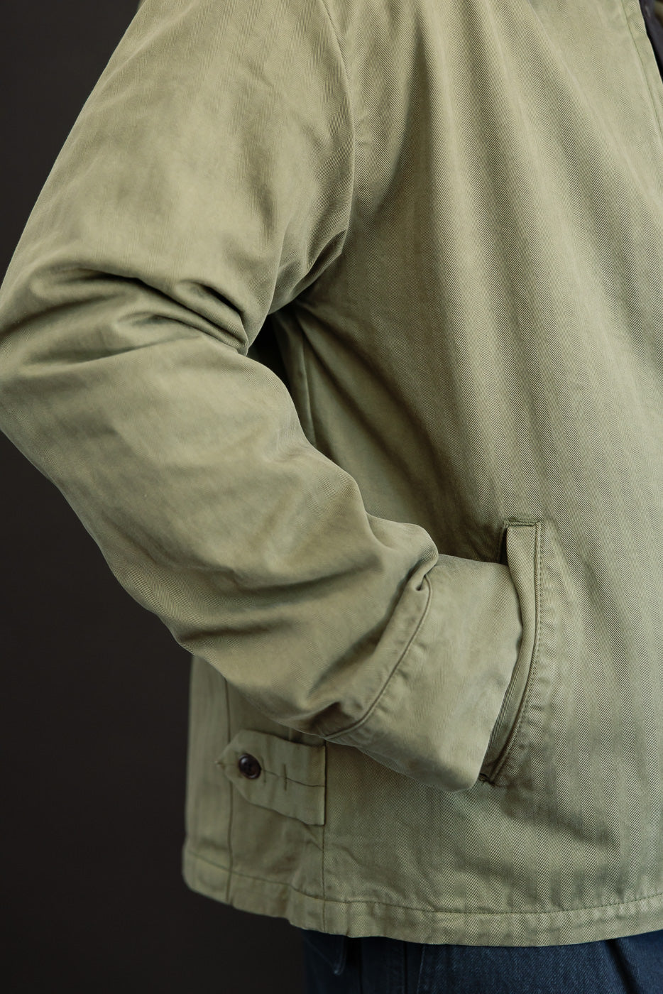 Close-up side view of a male model's olive green canvas jacket, showing the sleeve and pocket detail.