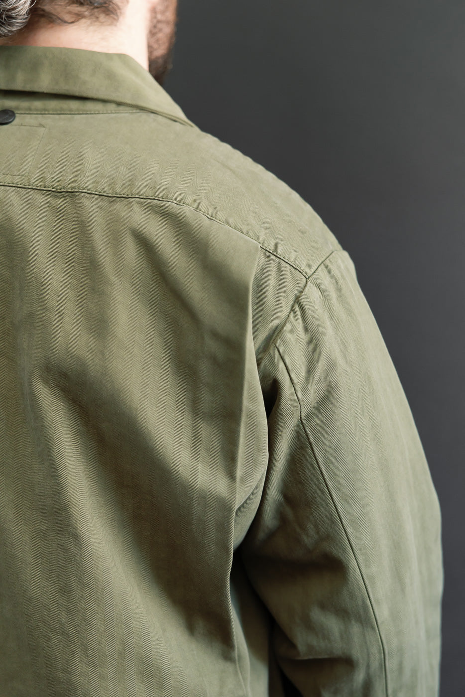 Close-up back view of an olive green cotton twill shirt showing shoulder seam and sleeve detail.