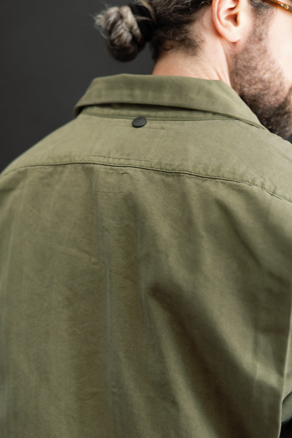 Close-up back view of an olive green cotton shirt showing collar and button detail on a male model.
