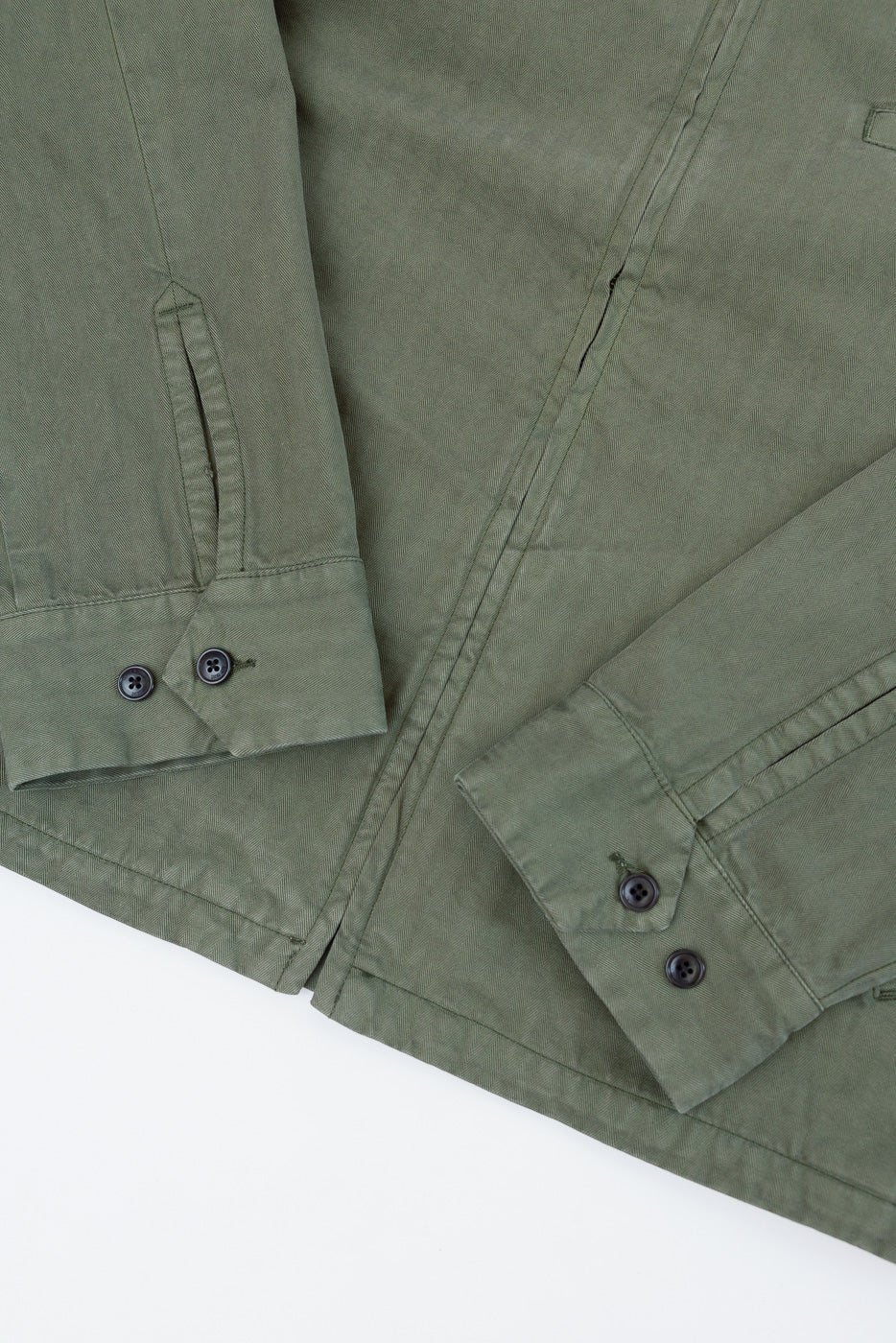 Close-up front view of olive green fabric texture and buttoned cuffs on a long-sleeve shirt.
